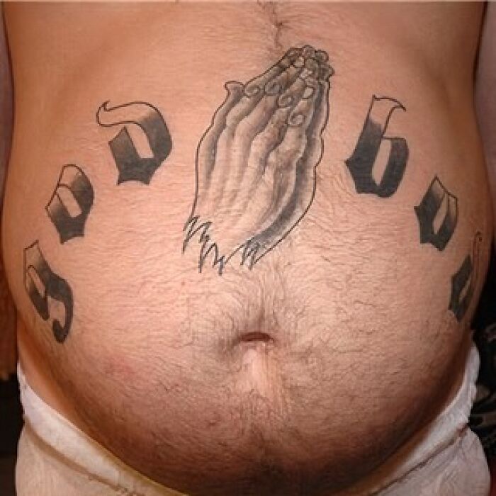 Tatuaje de manos rezando en abdomen con letras negras grandes en círculo, ejemplo de tatuajes horribles que no notan.