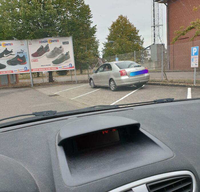 Coche mal estacionado ocupando varias plazas en un aparcamiento, mostrando ignorancia de normas básicas de educación.