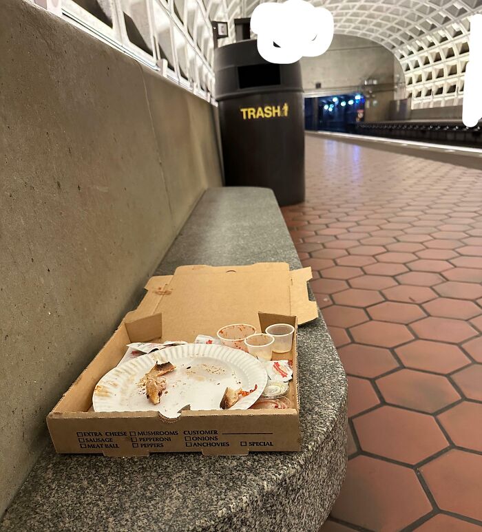 Restos de pizza y basura abandonados en banco de estación, ejemplo de ignorantes sin normas básicas de educación ni vergüenza.