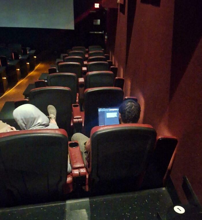 Personas en cine ignorando normas básicas de educación usando laptop en la sala mientras inicia la película.
