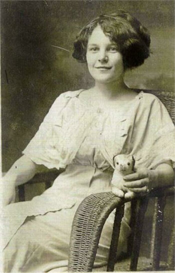 Mujer de hace décadas sentada en silla de mimbre con un peluche vintage, foto histórica elocuente.