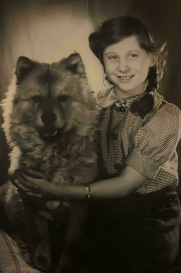 Niña sonriente abrazando a un perro peludo en foto antigua en blanco y negro, ejemplo de fotos de hace décadas.