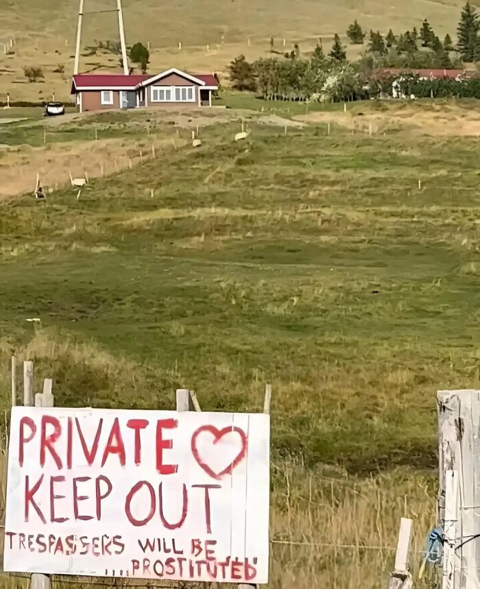 Cartel con afirmación incorrecta divertida en inglés sobre propiedad privada en campo abierto con casa al fondo.