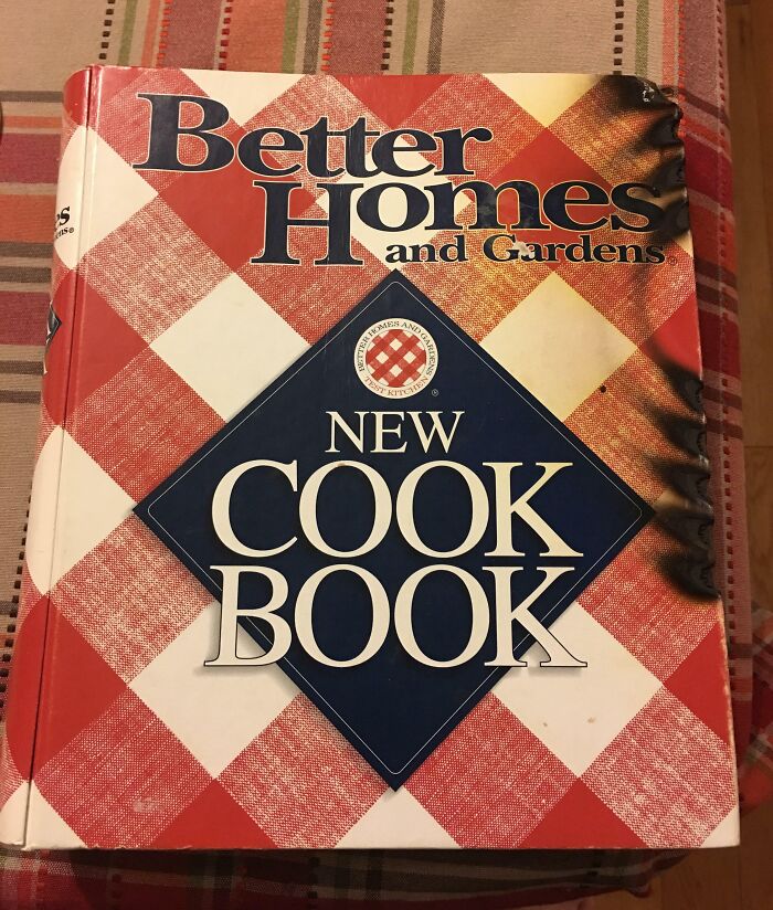Libro de cocina con cubierta quemada sobre un mantel a cuadros, representando personas que llevan un día peor que el tuyo.