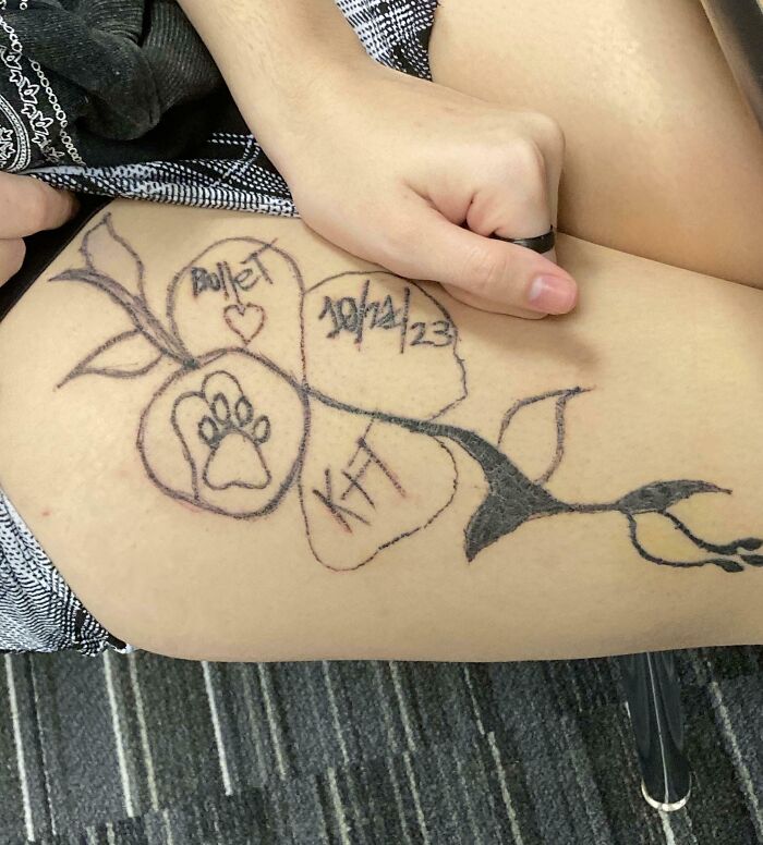 Tatuaje de mala elección en el muslo con diseño de corazón, fecha, huella de perro y nombres escritos a mano.