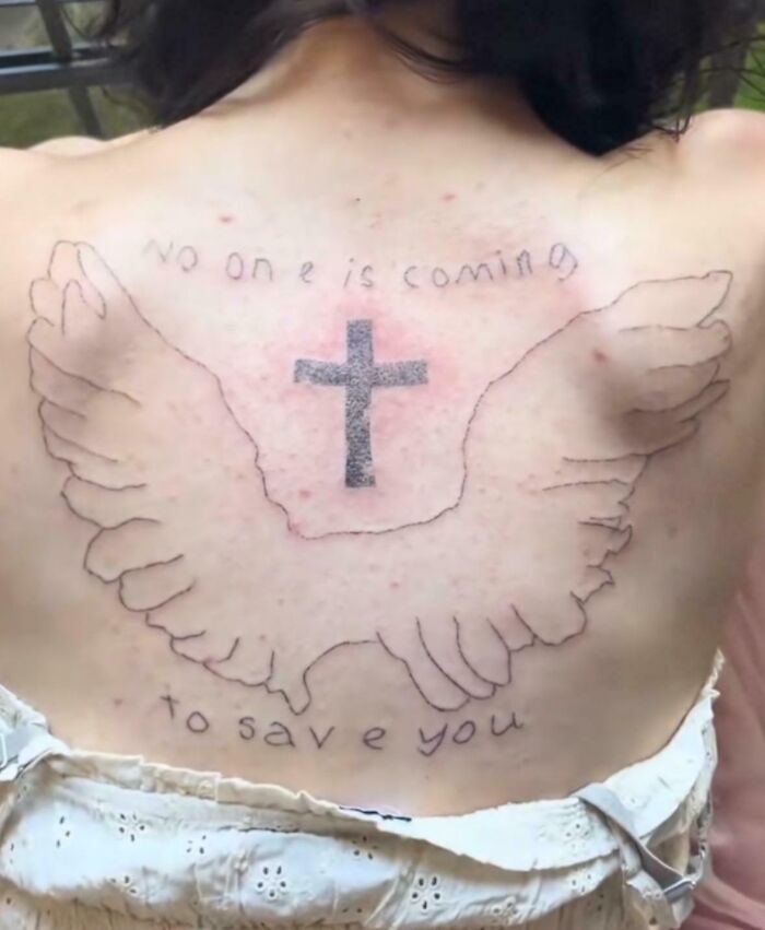 Tatuaje en la espalda con alas, cruz y texto mal hecho, ejemplo claro de tatuajes que fueron una mala elección.