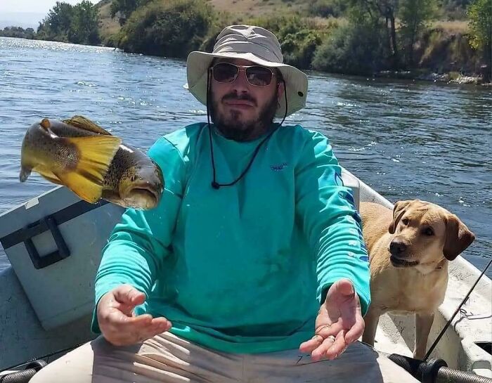 Hombre en bote con perro observa pez flotando en el aire, una coincidencia increíble en un día de pesca.