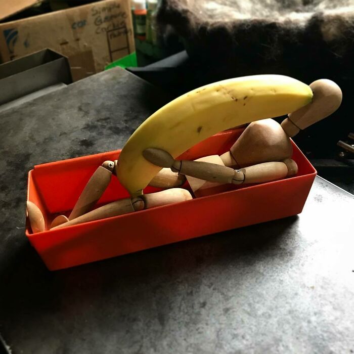 Muñeco de madera con plátano en caja roja, creando una escena divertida.