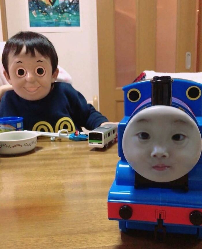Niño con rostro editado sentado en mesa junto a un tren azul con cara humana, imagen maldita difícil de explicar.