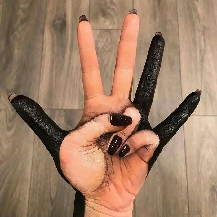Mano con tatuaje inusual, dedos pintados de negro, creando un diseño intrigante en el suelo de madera.