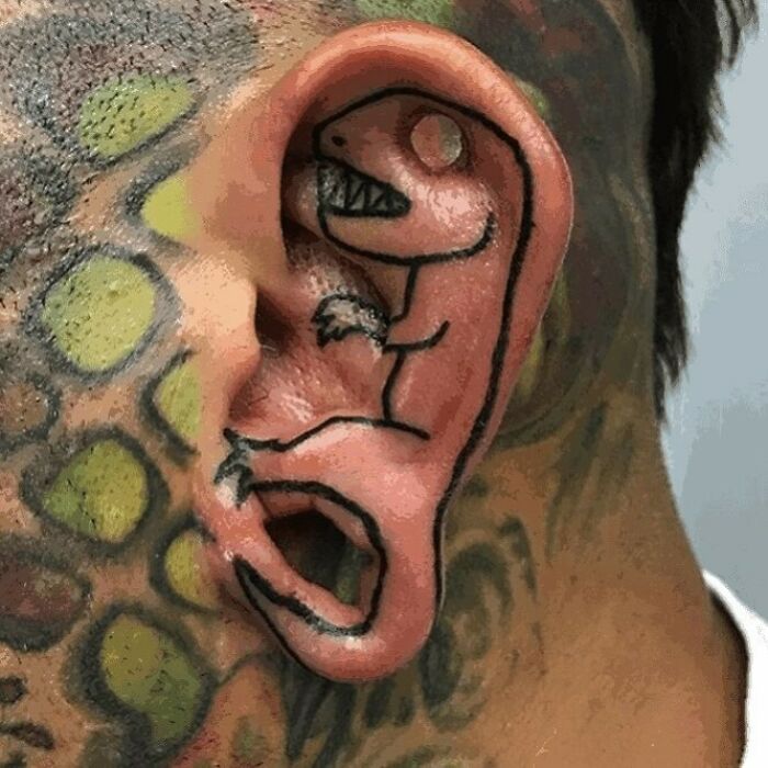 Tatuaje de dinosaurio en oreja de persona con otros tatuajes, ejemplo de tatuajes horribles que no se dan cuenta.