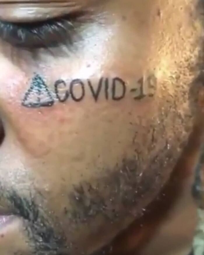 Tatuaje facial con texto COVID-19 y símbolo, ejemplo de tatuajes horribles que muchas personas no reconocen como malos.