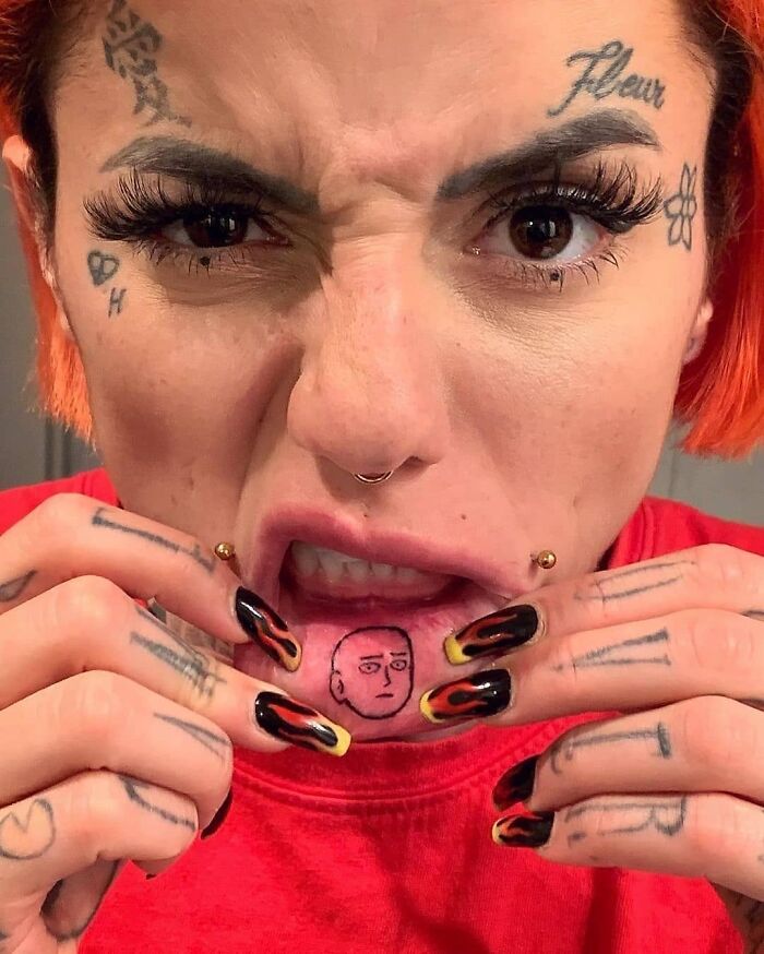 Mujer mostrando tatuaje curioso en el labio, arte corporal visible en la cara y manos.