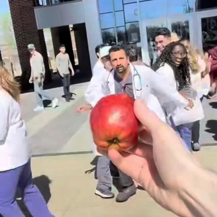 Mano sosteniendo una gran manzana roja frente a un grupo de personas sorprendidas, imagen maldita inexplicable.