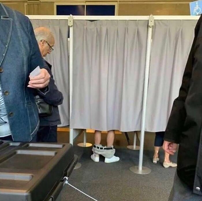 Piernas visibles bajo cortina en un lugar público con personas esperando, imagen maldita difícil de explicar.
