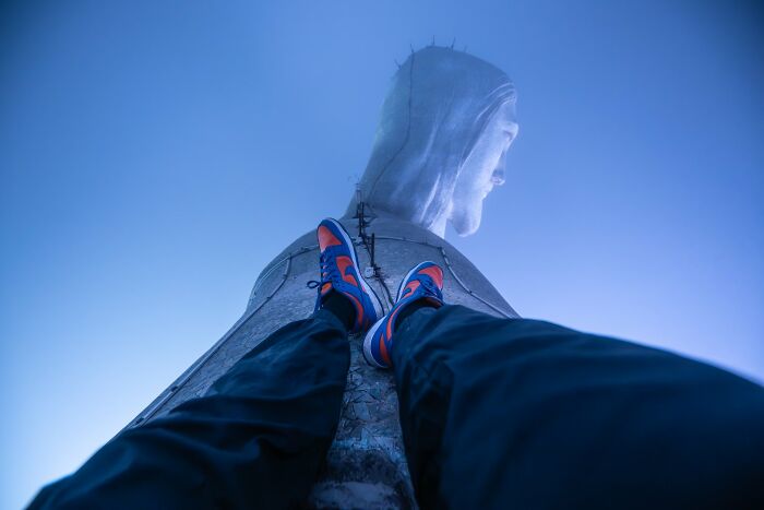 Vista desde abajo de persona con zapatillas sobre estatua gigante, foto curiosa que muestra otra perspectiva.