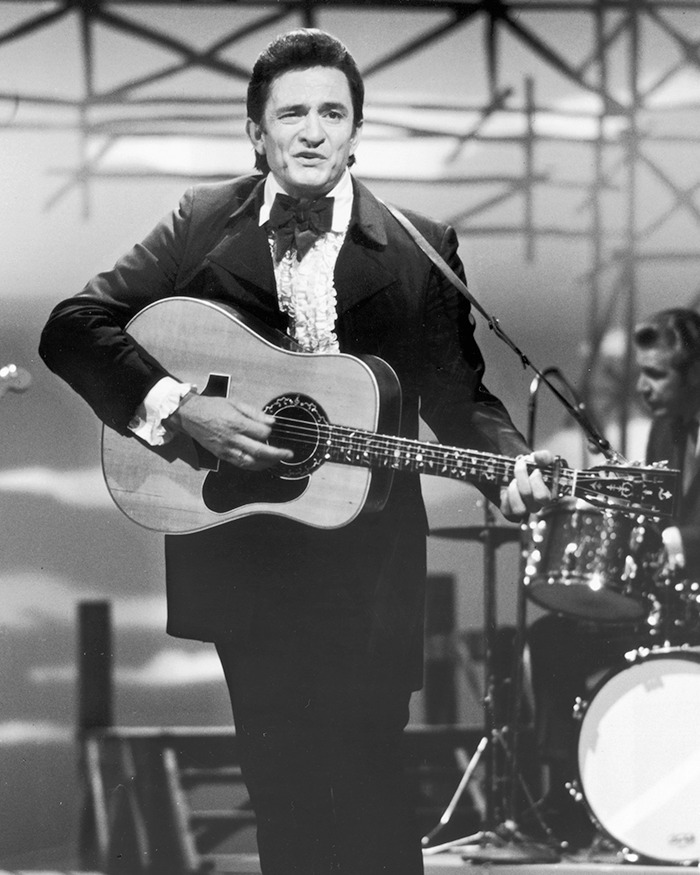 Celebridad tocando guitarra en escenario, vestido formalmente, resaltando notorios escándalos de celebridades.