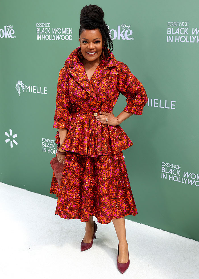 Mujer en alfombra roja con vestido estampado rojo, fondo verde en evento 