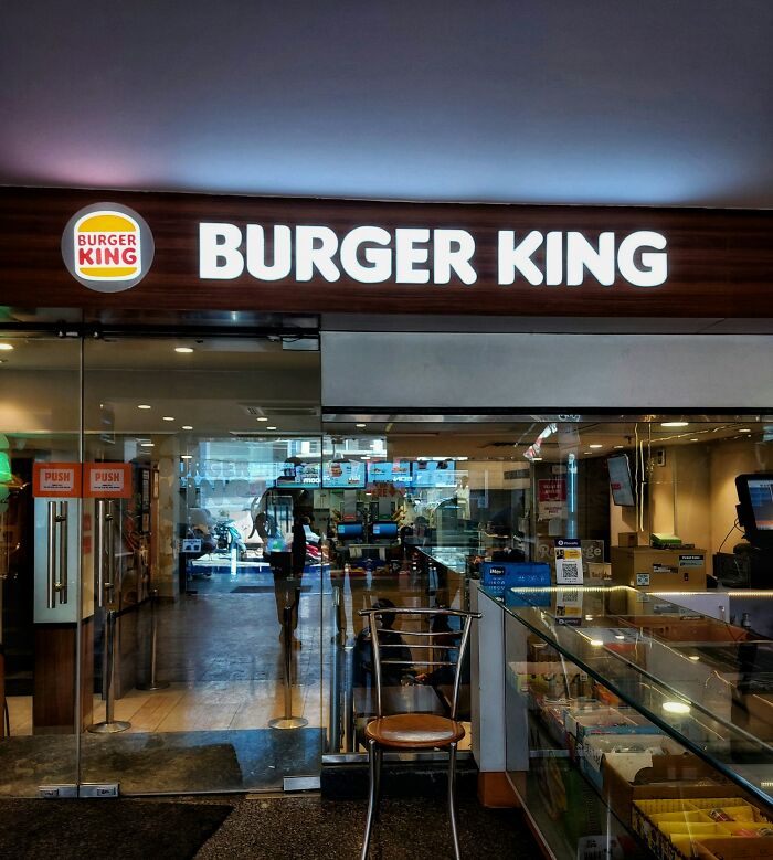 Entrada de Burger King con puertas de vidrio, mostrando interior vacío y reflejos en una tarde tranquila. Persona lista para irse.