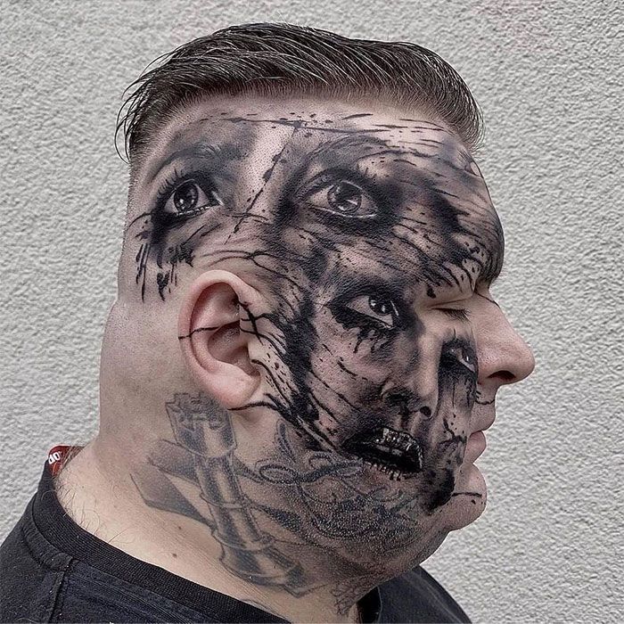 Hombre con tatuajes faciales complejos y oscuros que cubren toda la cabeza.