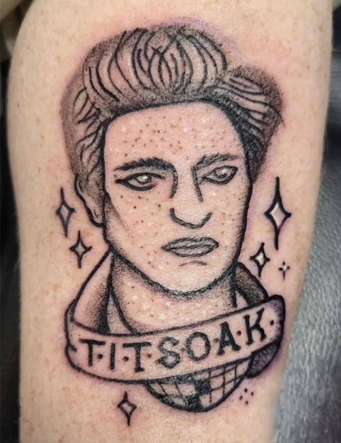 Dibujo de tatuaje con rostro y texto en el brazo, mostrando líneas y detalles notables del arte del tatuaje.