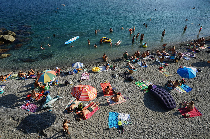 Playa llena con gente disfrutando del sol, toallas y sombrillas coloridas; ejemplo de choque cultural en veraneo.
