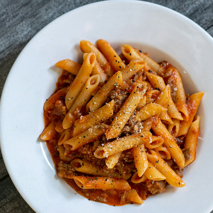 Pasta penne con salsa de tomate y carne en un plato blanco, destacado en choques culturales inesperados.