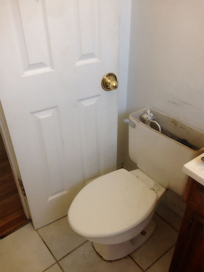 Puerta de baño bloqueada por inodoro mal colocado, mostrando reparación empeorada.