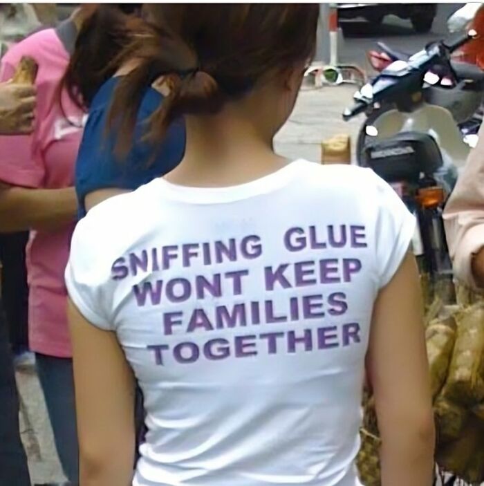 Mujer de espaldas con camiseta blanca divertida y ridícula con texto en inglés en un entorno urbano con gente alrededor.