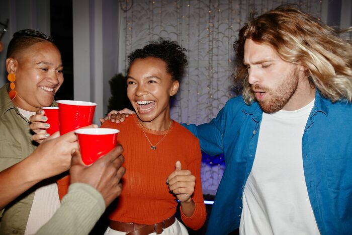 Grupo de personas en fiesta con vasos rojos disfrutando mientras alguien siente que debe irse ya mismo.
