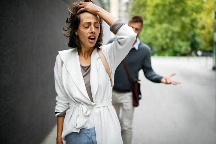 Mujer preocupada tocándose la cabeza mientras discute con su pareja en la calle, reflejando momentos de ruptura sentimental.