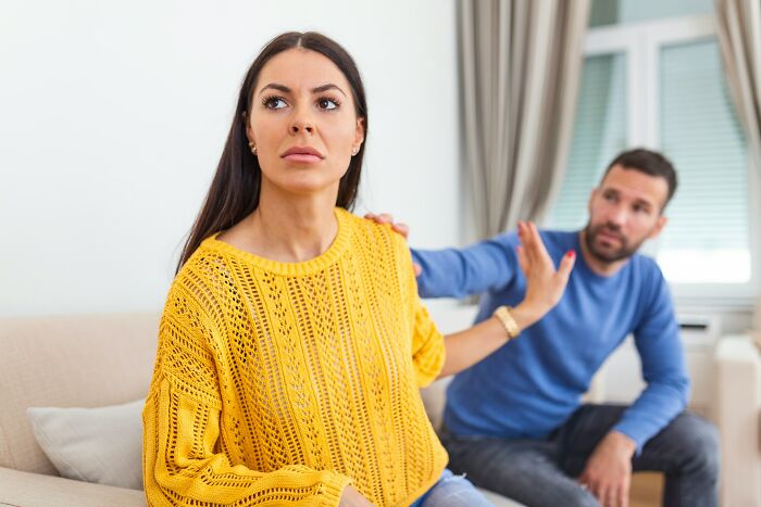 Mujer con suéter amarillo alejándose con gesto firme mientras hombre intenta acercarse, momentos de ruptura y desilusión en pareja.
