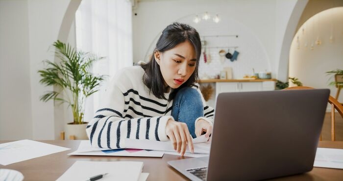 Mujer pensativa revisando documentos frente a laptop, reflejando momentos en que mujeres se dieron cuenta de que no se casarían.