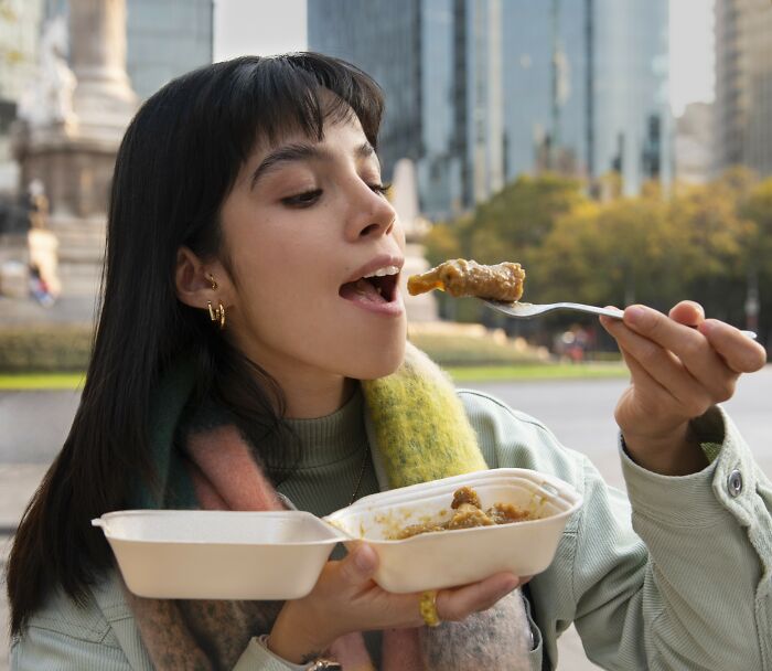 Mujer comiendo al aire libre, disfrutando comida para llevar, destacando actividades y objetos con peligro oculto.