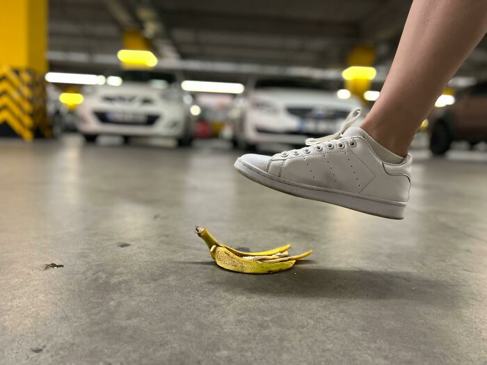Pie de foto de zapatilla blanca a punto de pisar una cáscara de plátano en estacionamiento, objeto aparentemente inofensivo peligroso.