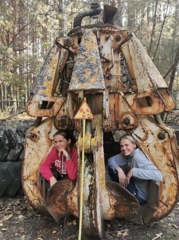Personas posan dentro de maquinaria oxidada en el bosque, sin notar un peligroso signo radiactivo.
