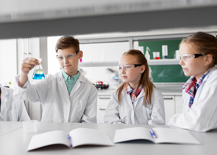 Estudiantes en laboratorio, ignorando advertencias, observan un frasco azul durante el experimento.