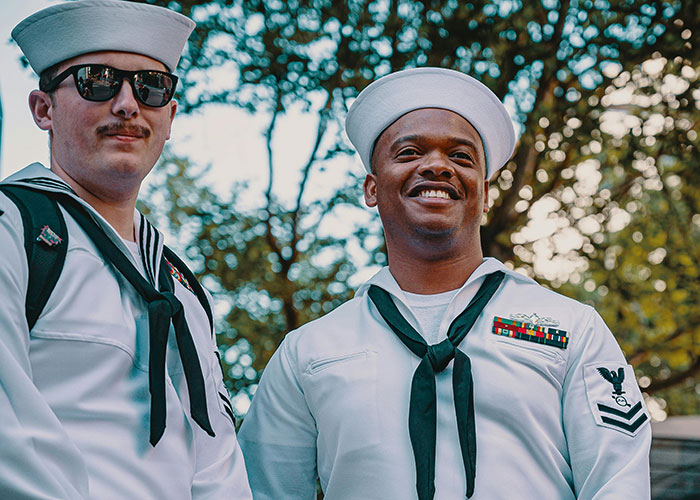 Marineros en uniforme blanco sonriendo, luces y sombras en un ambiente de bosque.