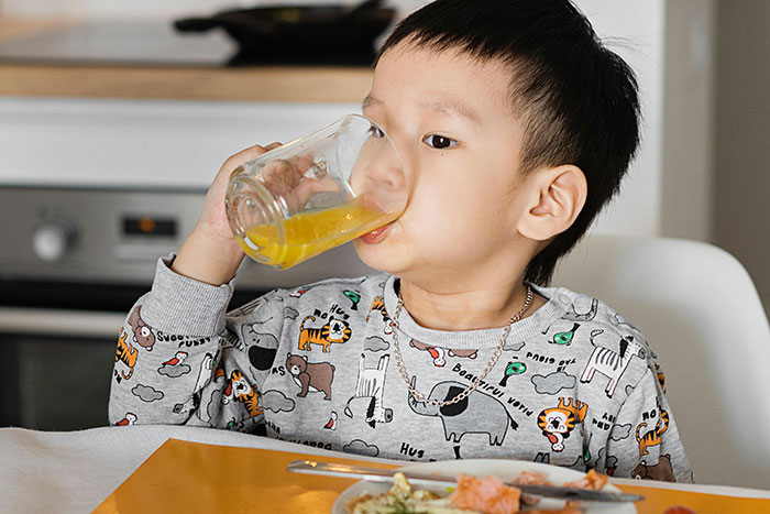 Niño pequeño bebiendo jugo en la cocina, mostrando actitud preventiva para evitar accidentes o tragedias.