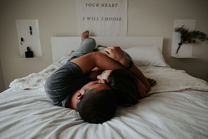Pareja abrazada en cama blanca, mostrando cuidado y protección como símbolo de prevención y acciones por si acaso.