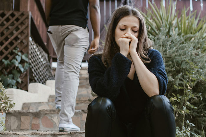 Mujer pensativa sentada en escaleras mientras hombre se aleja, representando prevención y acción por si acaso.