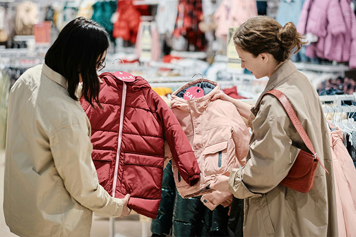 Dos mujeres comparando chaquetas en tienda de ropa durante una venta, mostrando fascinantes datos que sorprenden la realidad.