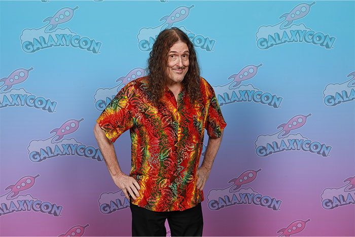Hombre con camisa colorida posando frente a fondo de GalaxyCon, ilustrando curiosidades de Hoy aprendí datos fascinantes.