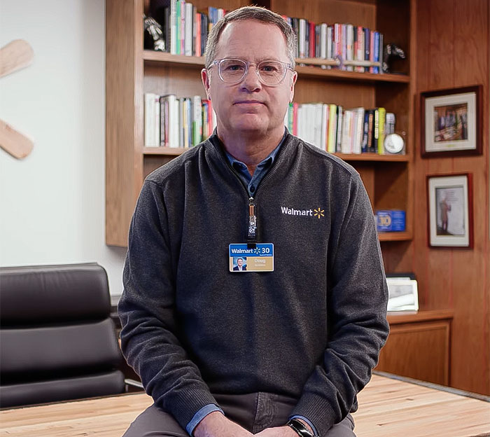 Man in a Walmart sweater with an ID badge, seated in an office setting.