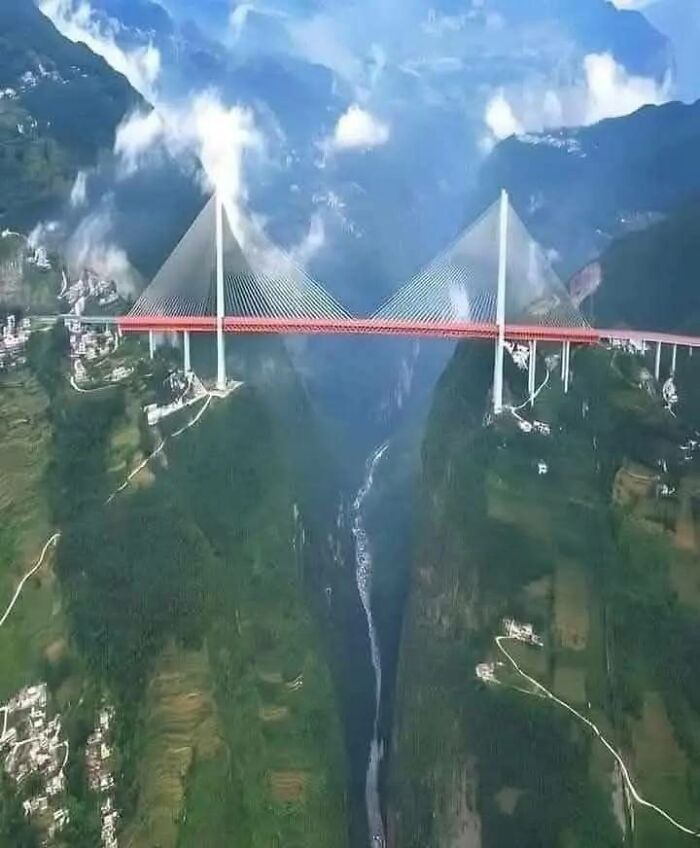 Puente colgante rojo sobre un profundo cañón entre montañas verdes, uno de los lugares misteriosos encontrados en Google Earth.