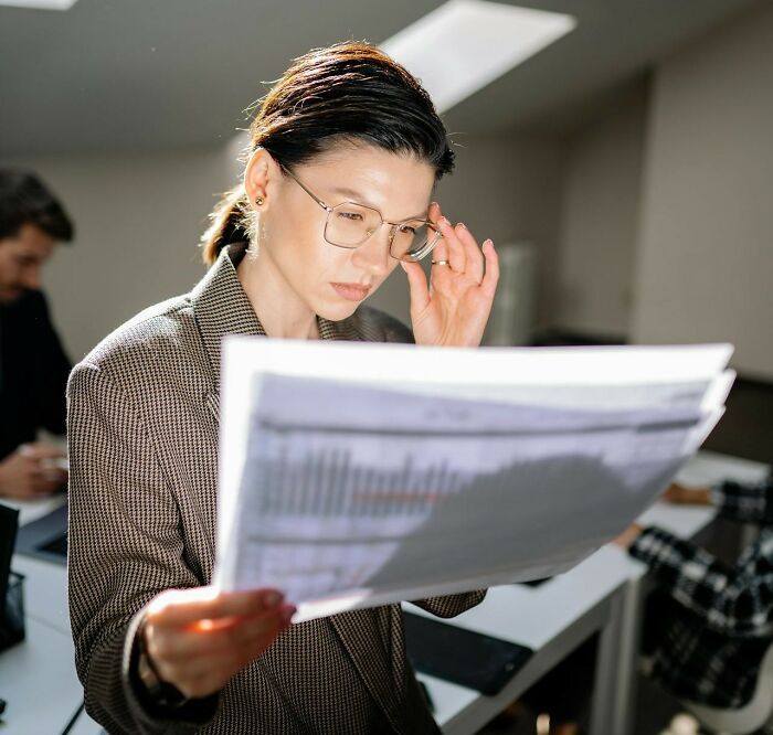 Mujer con gafas leyendo información en papel, aplicando trucos vitales útiles para su día a día en oficina moderna.