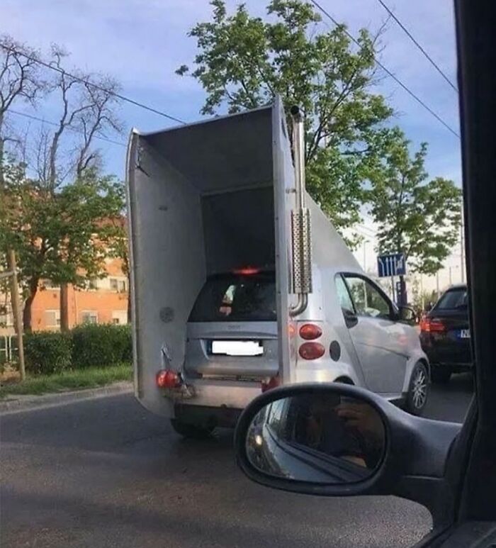 Carro pequeño dentro de una caja de camión más grande en la calle, imagen maldita a todos los niveles.
