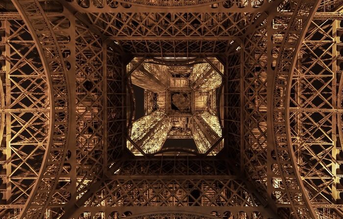 Foto curiosa de la estructura de la Torre Eiffel vista desde abajo mostrando perspectiva única y detalles metálicos iluminados.