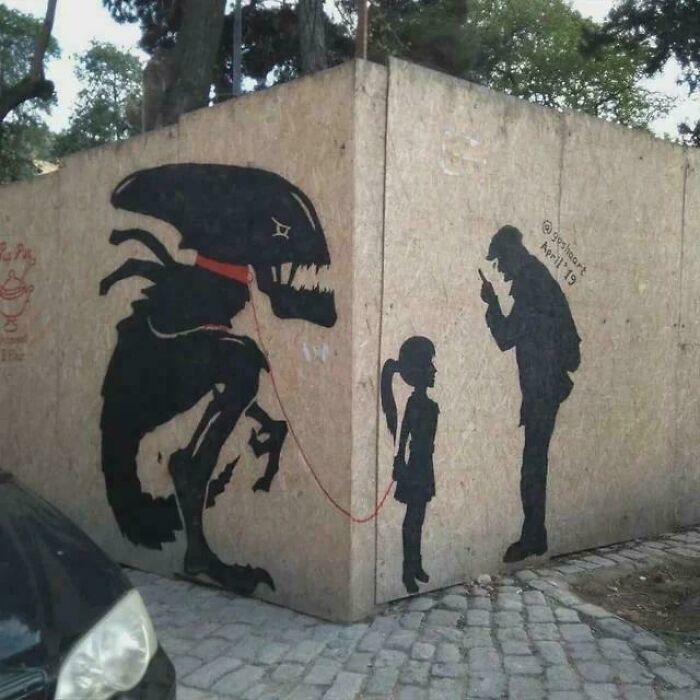 Grafiti en esquina mostrando imágenes bendecidas y malditas con niña, monstruo y hombre con celular en gesto amenazante.
