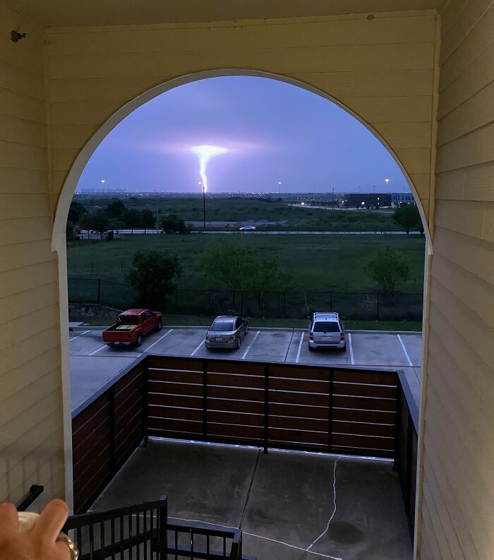 Vista desde un balcón con coincidencia increíble de un rayo iluminando el cielo en un paisaje urbano al atardecer.